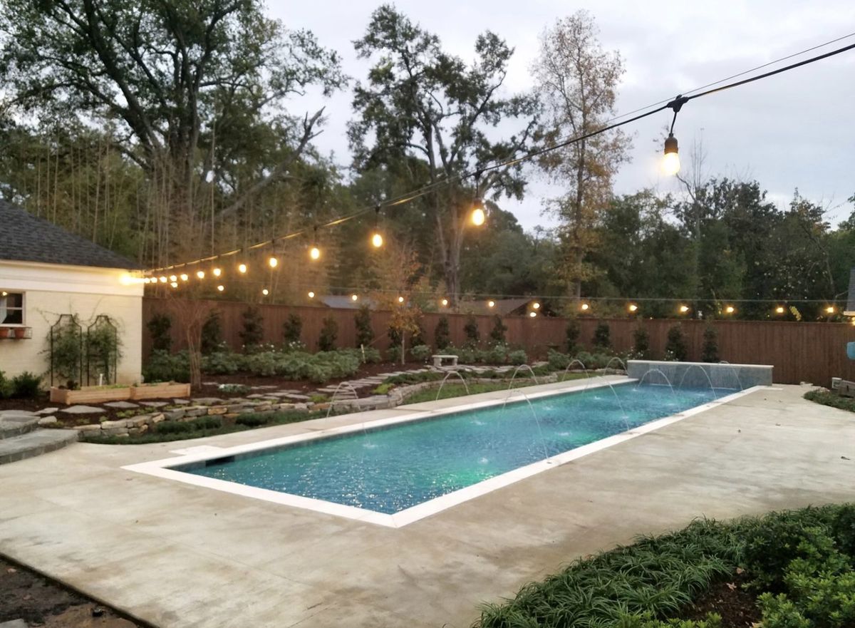 Rectangular pool with bubbler jets, string lights, and garden landscaping at dusk