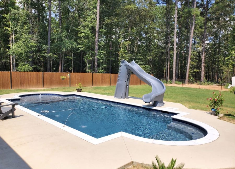 Custom pool with waterslide and attached spa surrounded by landscaping